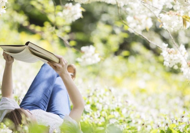 Woman reading book in grass under tree with white blossoms